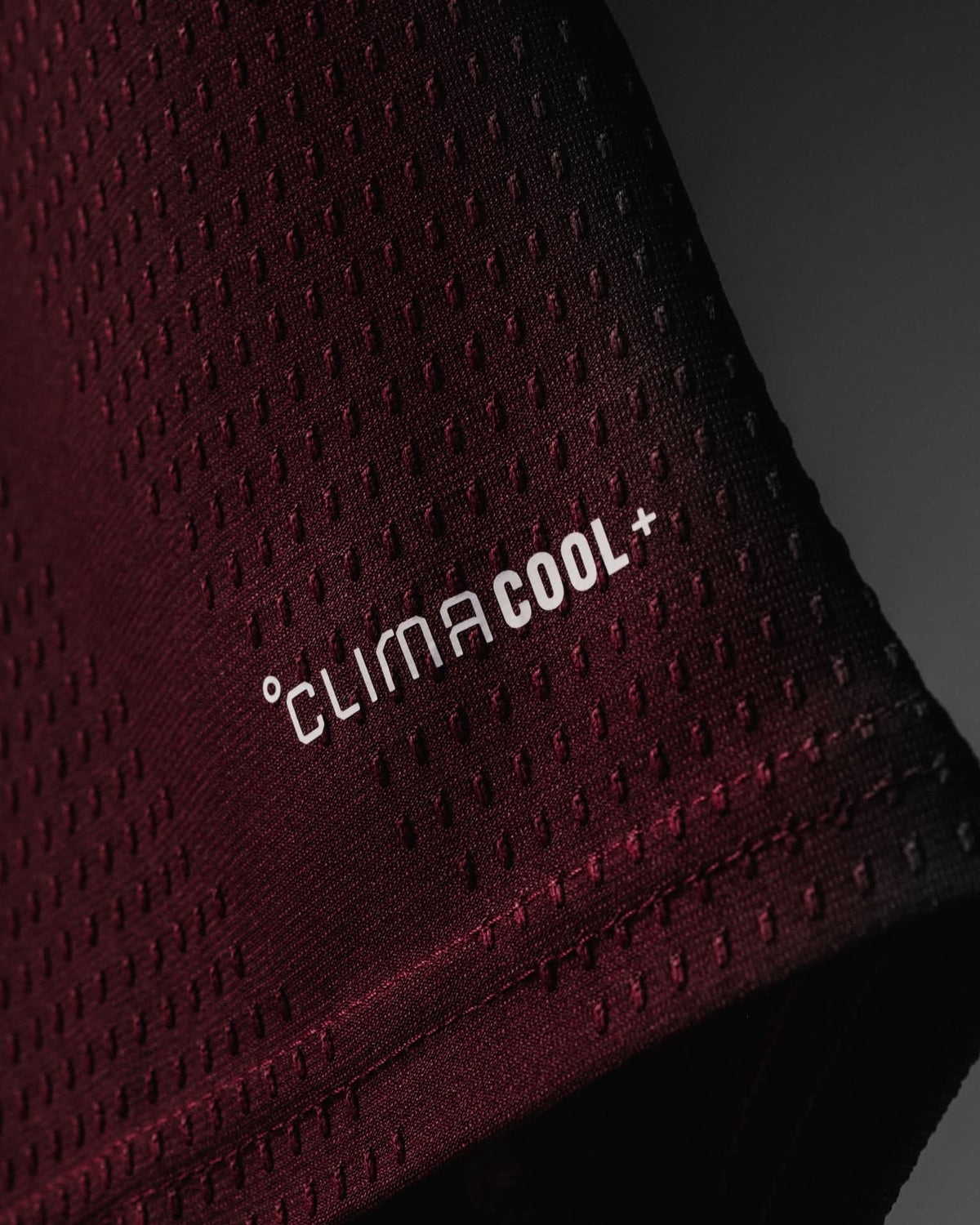 Close-up of a dark burgundy athletic mesh fabric with a white 'CLIMA COOL+' logo printed on the side, showing the textured knit pattern and stitched edge.